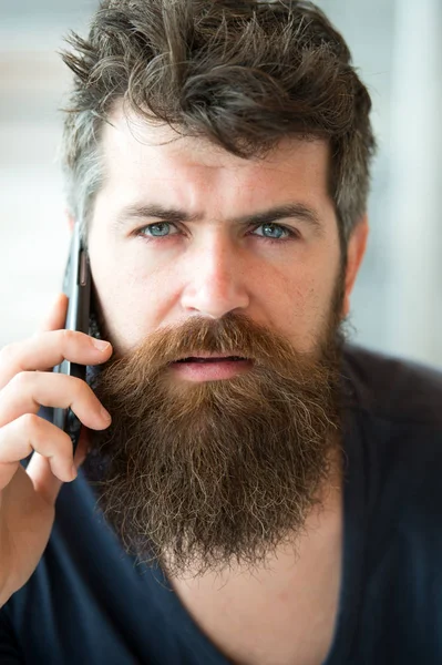 El hombre barbudo sostiene el teléfono móvil. Hipster barbudo comunicar llamada de teléfono inteligente. Comunicación móvil. Concepto de comunicación. Hombre con barba y bigote conversación de teléfono móvil fondo desenfocado — Foto de Stock