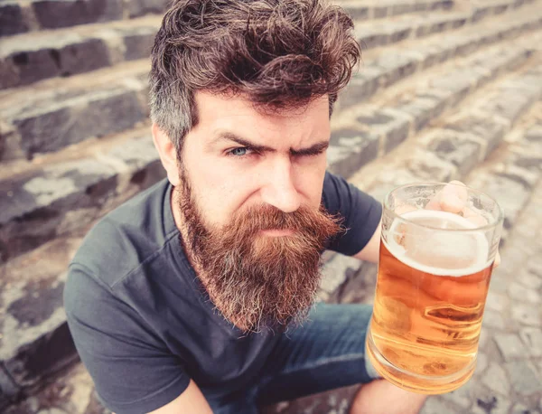 Hipster na ścisłe twarz picie piwa na zewnątrz, podniesienie napój. Koncepcja okrzyki. Człowiek z broda i wąsy posiada szkło z piwem, podczas gdy siedzi na kamienne schody. Facet po odpoczynku z zimne piwo — Zdjęcie stockowe