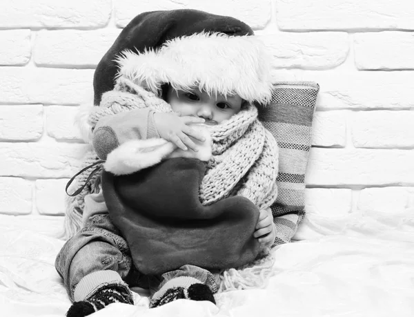 Mały chłopczyk z adorable curious oblicze w czerwonym swetrze z manekina w nowy rok Czapka szalik i Boże Narodzenie lub xmas Pończocha lub rozruchu na tle ściany Cegła biała — Zdjęcie stockowe