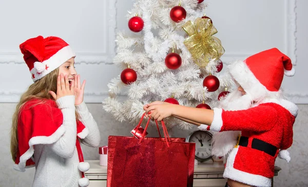 Niño vestido de santa con barba artificial blanca y sombrero rojo dar caja de regalo a la niña. Papá Noel trae regalos. Desempaquetar regalos de Navidad. Feliz navidad. Los niños celebran la Navidad con regalos —  Fotos de Stock