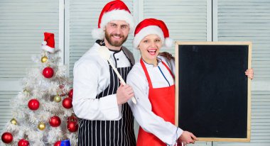 Erkek ve kadın şef santa şapka Noel ağacı yakınındaki blackboard kopya alanı tutun. Noel yemeği için çift onay listesi malzemeler. Christmas yemek yemek. Noel tarifi kavramı. Bizim aile için menü