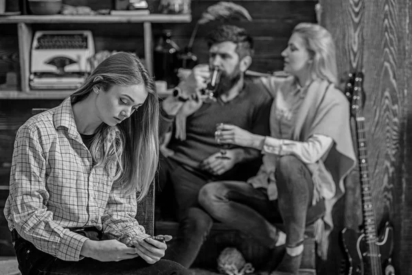 Teenager absorbed with gadget and not talking to parents, generation gap, rebellious youth concept. Bearded man and blond woman having lovely chat while their daughter is texting friends over phone