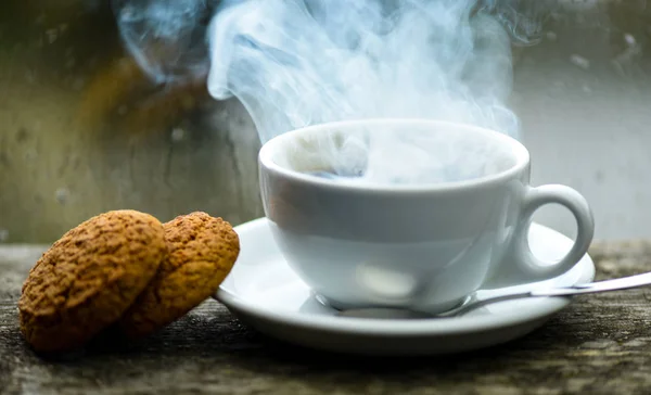 Enjoying coffee on rainy day. Coffee time on rainy day. Fresh brewed coffee in white cup or mug on windowsill. Wet glass window and cup of hot caffeine beverage. Coffee drink with oat cookies dessert.