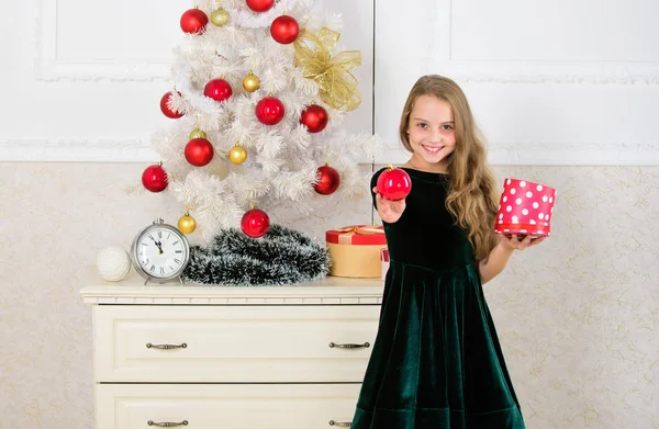Традиционный семейный праздник. Девочка возле рождественской елки держит подарочную коробку. Ребенок празднует Рождество дома. Любимый день года. Пора открывать рождественские подарки. Открытие рождественских подарков — стоковое фото