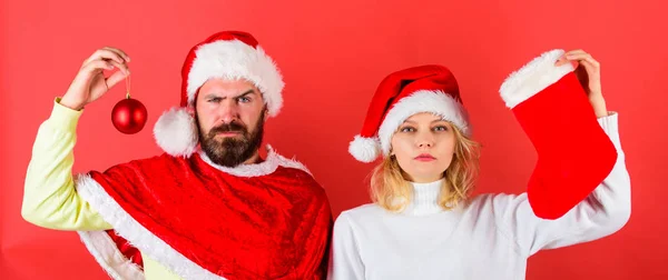 Concept de célébration de Noël. Femme et homme barbu en chapeau de Père Noël attendant fond rouge de Noël. Tradition de bas de Noël. Couple Noël santa costume tenir chaussette et ornement balle — Photo