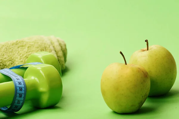 Haltères de couleur vert vif, ruban à mesurer, serviette et fruits — Photo