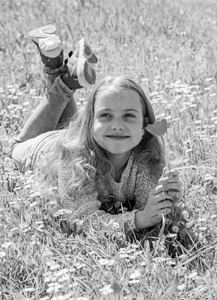 Mädchen mit langen Haaren auf Grasfläche liegend, Grashintergrund. Frühlingshafte Stimmung. Kinder genießen frühlingshaftes sonniges Wetter auf der Wiese. Mädchen auf lächelndem Gesicht hält rote Tulpenblume — Stockfoto