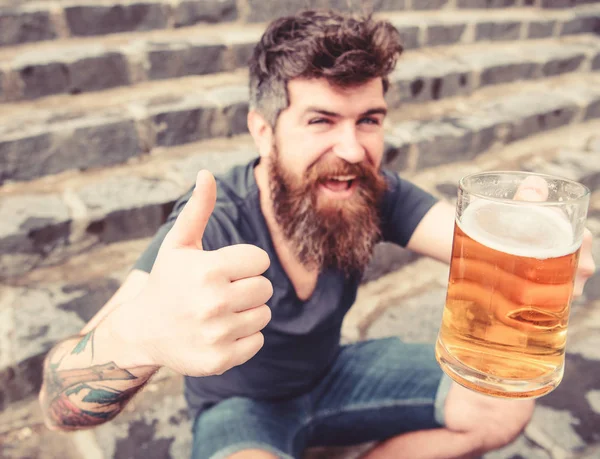 Człowiek z broda i wąsy posiada szkło z piwa i pokazuje kciuk w górę, schody kamienne podłoże. Koncepcja piwa z beczki. Facet po odpoczynku z piwem, Selektywny fokus. Hipster na wesołą twarz pije piwo — Zdjęcie stockowe