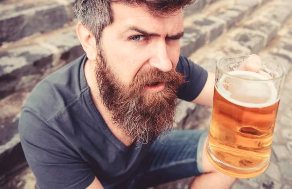 Człowiek z broda i wąsy posiada szkło z piwem, podczas gdy siedzi na kamienne schody, rozmyte. Facet, podnoszenie się szkło z piwa z beczki. Hipster na ścisłe twarz pije piwo odkryty. Koncepcja celebracja — Zdjęcie stockowe