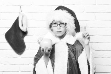 Noel Baba 'nın kırmızı gözlüklü genç ve yeni yıl şapkalı dekoratif noel ya da xmas çoraplı ya da elinde beyaz tuğlalı arka planda parmak kaldırmış pembe domuz kumbaralı yakışıklı çocuğu.