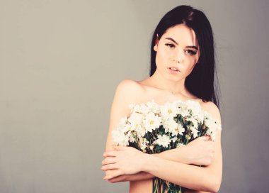 Kadın göğüslerini buket kapaklarla gizleme. Bayan göğüsler çiçekler, gri arka plan ile kapsar. Kanser meme kavramının. Sakin yüz çıplak kız papatya çiçeği göğüs önünde tutar..