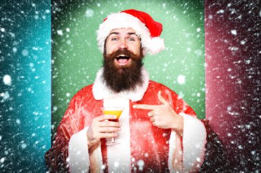 alkollü içecek bardak Noel veya xmas kazak ve yeni yıl şapka tutan yüz gülümseyen üzerinde uzun sakallı yakışıklı sakallı Noel Baba adam üzerinde renkli stüdyo arka plan üzerinde gösterir