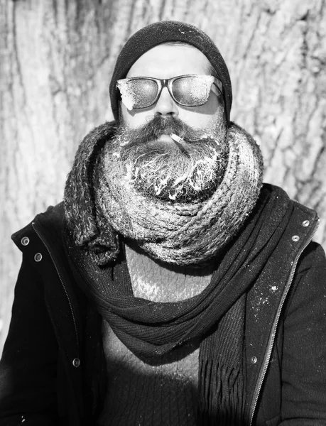 Stilig skäggig man, hipster, med skägg och mustasch i svarta solglasögon täckt med vit frost röker cigarett på vinterdag utomhus på naturliga bak — Stockfoto