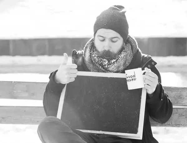 잘생긴 놀된 남자, 수염 및 콧수염 화이트 프 로스트, 덮여 hipster 빈 블랙 보드를 보유 하 고 및 컵으로 좋은 아침 텍스트 자연 배경에서 겨울 날에, spac 복사 — 스톡 사진