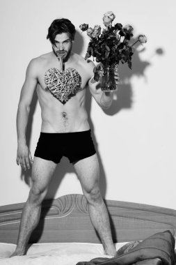 yakışıklı sakallı seksi maço erkek iç çamaşırı yatakta kırmızı battaniye holding turuncu gül yakınındaki şık sakal ayakta ve dekoratif Sevgililer kalp kas gövde atletik vücut üzerinde ile diş ile