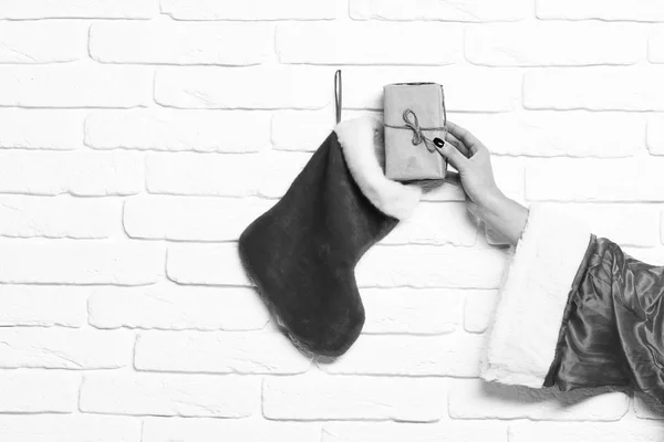Mano femenina se presenta envuelto en papel artesanal de la media de Navidad o bota de Navidad en fondo de pared de ladrillo blanco — Foto de Stock