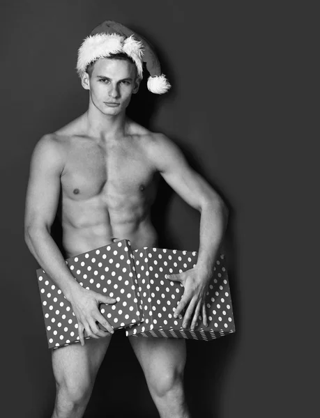 Junge hübsche Macho-Weihnachtsmann mit sexy muskulösen athletischen starken Körper hat nackten Oberkörper und starken Bauch in Weihnachts- oder Weihnachtsmütze mit bunten Geschenkbox auf grünem Studiohintergrund bedeckt — Stockfoto