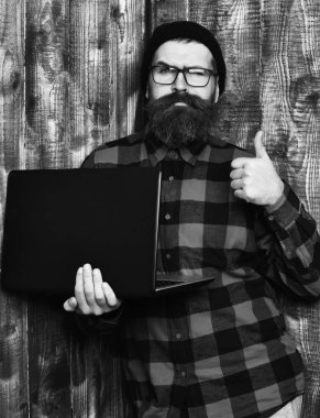 Sakallı adam, uzun sakal. Acımasız beyaz ciddi tıraşsız hipster dizüstü şapka ve gözlük kahverengi vintage ahşap studio adam kırmızı siyah damalı gömlek holding