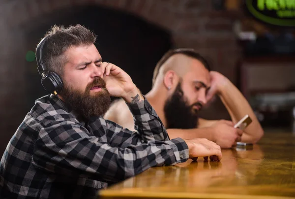 Order drinks at bar counter. Men with headphones and smartphone relaxing at bar. Avoid communication. Escape reality. Friday relaxation in bar. Hipster bearded man spend leisure at bar counter