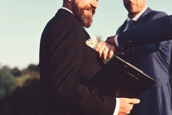 Man with beard and smiling face holds folder takes bribe.