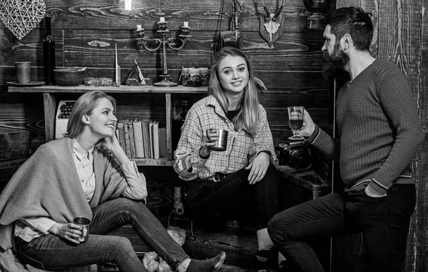 Familia disfrutar de la conversación en la casa de guardabosques. Amigos, familia pasar la noche agradable, fondo interior. Concepto de conversación sincera. Las niñas y el hombre en caras felices sostienen tazas metálicas, hablando —  Fotos de Stock