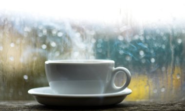 Taze yapılmış kahve beyaz fincan veya kupa pencere üzerinde. Islak cam pencere ve sıcak kahve. Sonbahar bulutlu hava kafein içecek ile daha iyi. Kahve yağmurlu günde zevk. Yağmurlu gün kahve saati