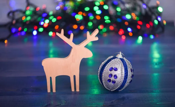 Bola con adornos y juguete de ciervo de madera sobre fondo de guirnalda colorido borroso. Decoración de Navidad. Símbolos de las vacaciones de invierno de Navidad. Ciervo y adorno decorativo de juguete. Feliz concepto de Navidad —  Fotos de Stock