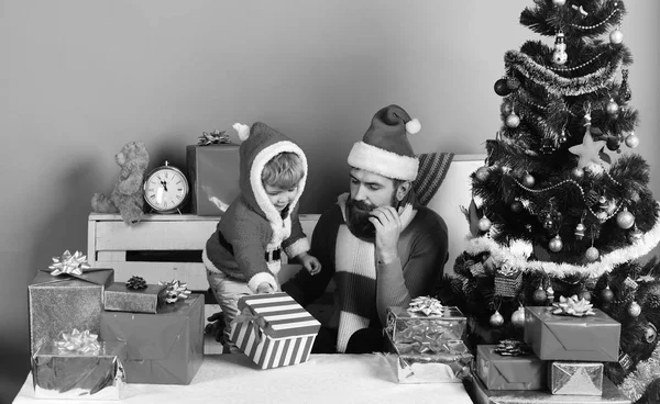 Père Noël et petit assistant parmi les coffrets cadeaux près de sapin. — Photo