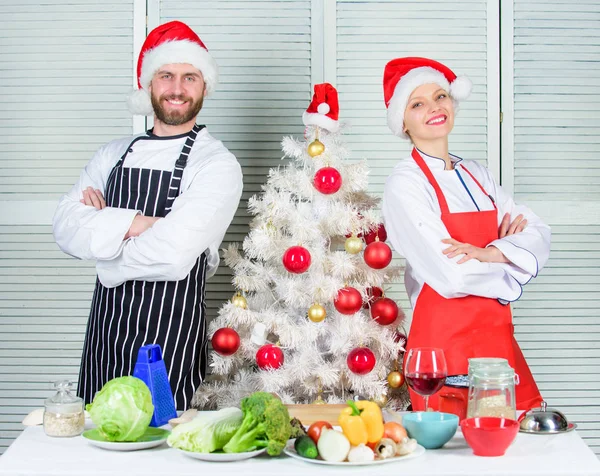 Couple preparing a healthy meal together for christmas dinner. Man and woman chef apron santa hat near christmas tree. Christmas recipe concept. Cooking christmas meal. Secret ingredient is love