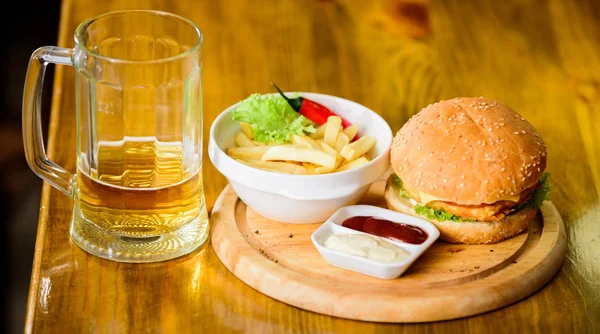 Hamburguesa con carne de queso y ensalada. Comida de bar y jarra de cerveza. Concepto de comida rápida. Menú de hamburguesas. Snack alto en calorías. Hamburguesa y papas fritas y salsa de tomate sobre tabla de madera. Deliciosa hamburguesa —  Fotos de Stock