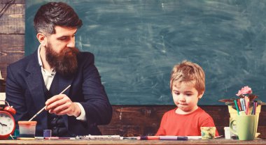 Çocuk ve meşgul yüz boyama, resim öğretmeni. Sanat ders kavramı. Sakallı öğretmeni, sınıfta, kara tahta arka plan çizmek için küçük oğlu baba öğretir. Yetenekli sanatçı oğlumla vakit geçirmek
