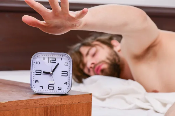 Cheerful young man is waking up after sleeping in the morning. Handsome man using clock in bed after waking up in the morning. Men in bed. — Stock Photo, Image