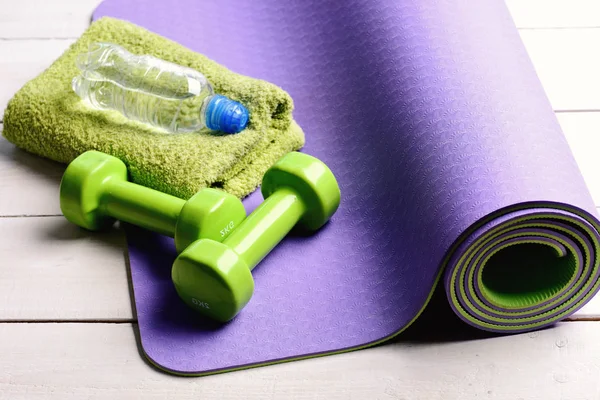 Barbells near water bottle and soft towel on yoga mat