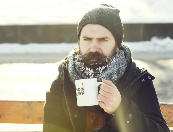 Homem carrancudo, hipster barbudo com barba e bigode coberto com bebidas de geada branca de xícara com texto de bom dia sentado em banco de madeira no dia de inverno nevado ao ar livre em backgroun natural — Fotografia de Stock