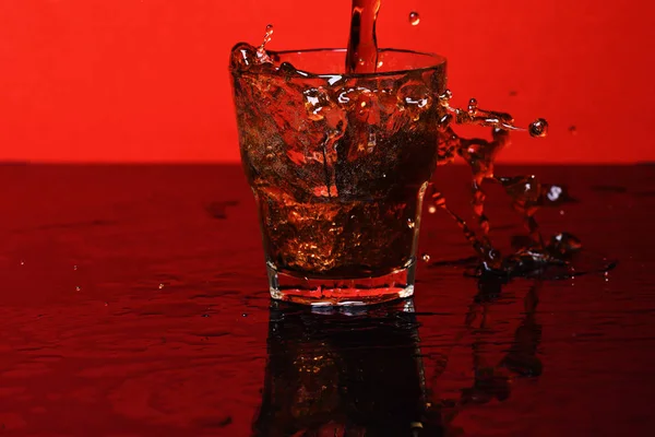 Splash of water in glass for whiskey on red background, side vie — стоковое фото