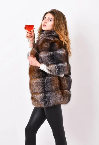 Wine culture concept. Woman drink wine. Girl fashion makeup wear fur coat hold glass alcohol. Elite leisure. Reasons drink red wine in wintertime. Lady fashion model curly hairstyle enjoy elite wine