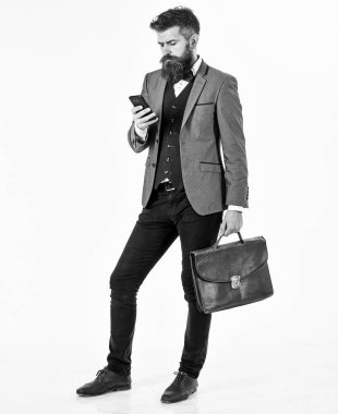 Acımasız adam meşgul görünüyor. Sakallı adam akıllı takım elbise giyiyor ve smartphone kullanır. Adam ciddi bir yüz, moda saç modeli ve evrak çantası. Başarı, iş, yeni tachnology, Internet, erkek moda kavramı