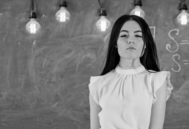 Beyaz bluz uzun saçlı kadın sınıfta durumda. Öğretmen ders, kopya alanı başlamak için hazır. Bayan öğretmen dalgın yüzünde kara tahta önünde duruyor. Elit okul kavramı