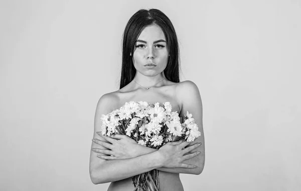 Mädchen mit ruhigem Gesicht steht nackt und hält Kamillenblüten vor der Brust. Dame bedeckt Brüste mit Blumen, isoliert auf grau. Hautpflegekonzept. Frau mit glatter, gesunder Haut sieht attraktiv aus — Stockfoto