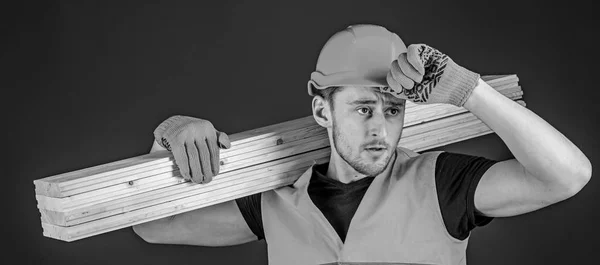 Bauarbeiter mit einer Holzplanke auf der Schulter. Tischler mit Schirmmütze, Schutzhandschuhen und orangefarbener Sicherheitsweste, blauem Hintergrund. Schutzausstattungskonzept — Stockfoto