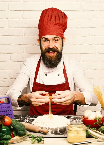 Koken met vrolijk gezicht in bordeaux uniform zit aan tafel — Stockfoto