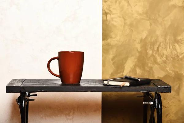 Concepto de lectura, escritura y educación. Una taza de bebida caliente y un cuaderno en una mesa pequeña. Taza de té o café y diario sobre fondo elegante. Bebida caliente y portátil en la mesa baja cerca de la pared — Foto de Stock