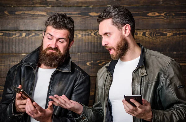 Men with smartphones surfing internet. Mobile internet. Business application. Men brutal bearded hipster in fashionable leather jackets use mobile internet. Online business. Modern technology