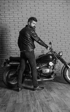 Erkeksi hobi kavramı. Yenilikçi, vahşi Motorcu deri ceket ciddi yüzüne üzerinde motosiklet üzerinde oturur. Sakallı, motorcu motorlu bisiklet garaj, tuğla duvar arka plan yakınındaki deri ceketli adam