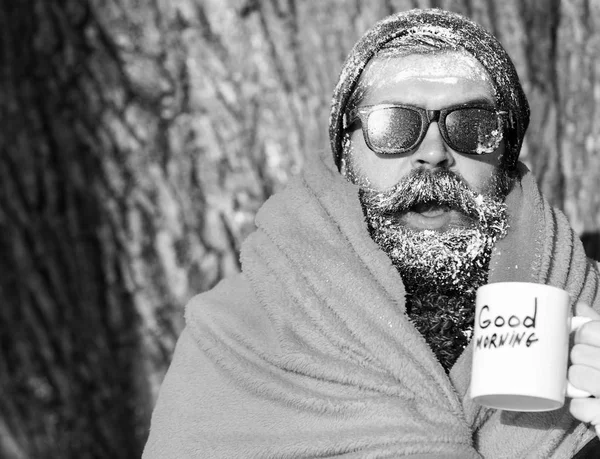 Homem animado congelado, hipster barbudo, com barba e bigode em óculos escuros pretos cobertos com geada branca envolta em cobertor laranja com bebida quente na xícara no dia de inverno no backgroun natural — Fotografia de Stock
