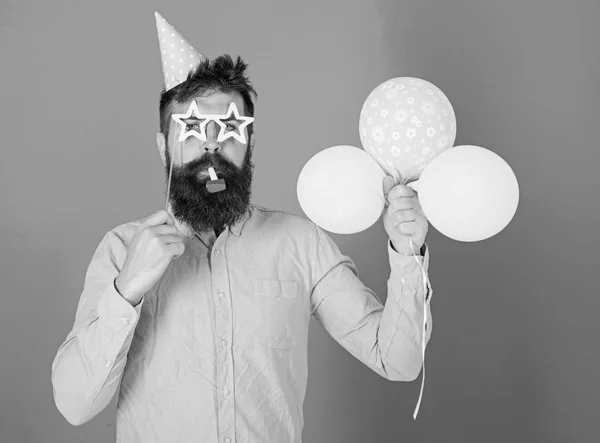 Άνδρας με γενειάδα στο ήρεμο πρόσωπο κατέχει αερόστατα, μπλε φόντο. Έκπληξη έννοια. Hipster στο star σχήμα γυαλιά χτυπήματα σε κόμμα κέρατο. Τύπος στο πάρτι καπέλο με διακοπές χαρακτηριστικά γιορτάζει — Φωτογραφία Αρχείου