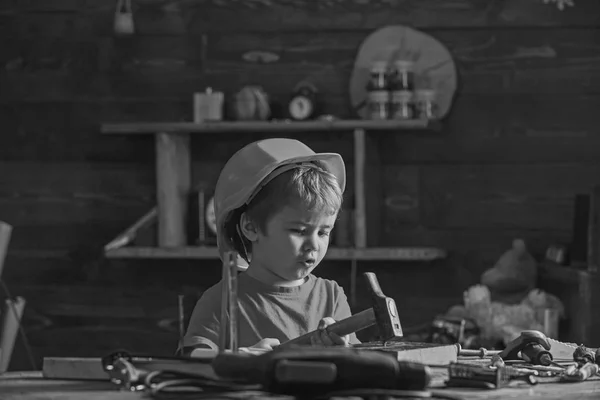 木製のブロックに釘を打っている間少年歌う歌。ワーク ショップの作業テーブルに座っている小さな子供 — ストック写真