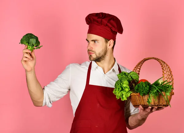 Koch in weinroter Uniform betrachtet Brokkoli. Vegetarisches Ernährungskonzept. — Stockfoto