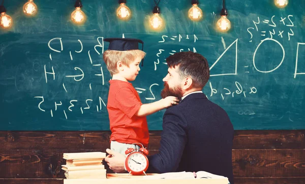 Boy, child in graduate cap play with dad, having fun and relaxing during school break. Teacher with beard, father teaches little son in classroom, chalkboard on background. School break concept — Stock Photo, Image