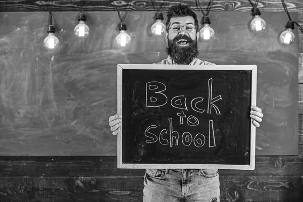 Γυμνάσιο έννοια. Άνδρας με μούσι και μουστάκι σε χαρούμενα χαμογελαστό πρόσωπο καλωσορίζει φοιτητές, chalkboard σε φόντο. Δάσκαλος σε γυαλιά κατέχει μαυροπίνακα με τίτλο πίσω στο σχολείο — Φωτογραφία Αρχείου